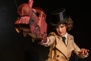 Une femme avec un chapeau haut de forme tient un train miniature.